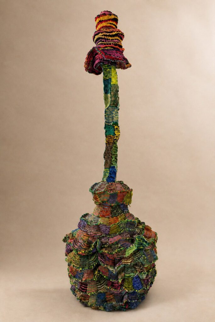 Tall stem rising from a patchwork vessel base. Pipe cleaner sculpture by Ted Fullwood