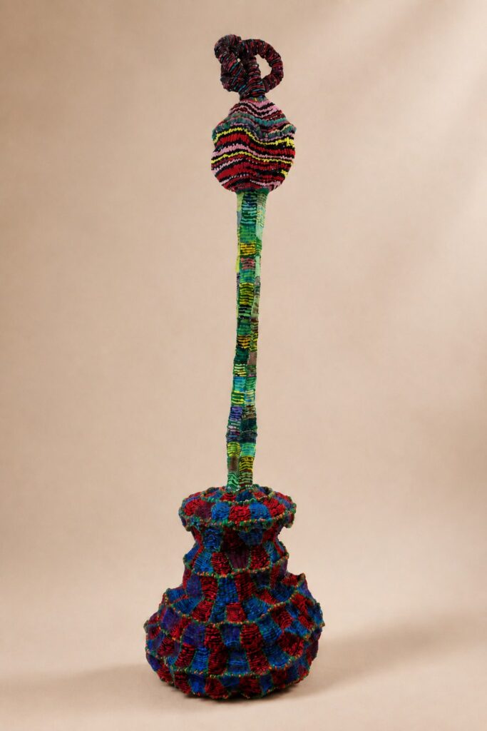 Slender stem on a red-and-blue vessel base. Pipe cleaner sculpture by Ted Fullwood