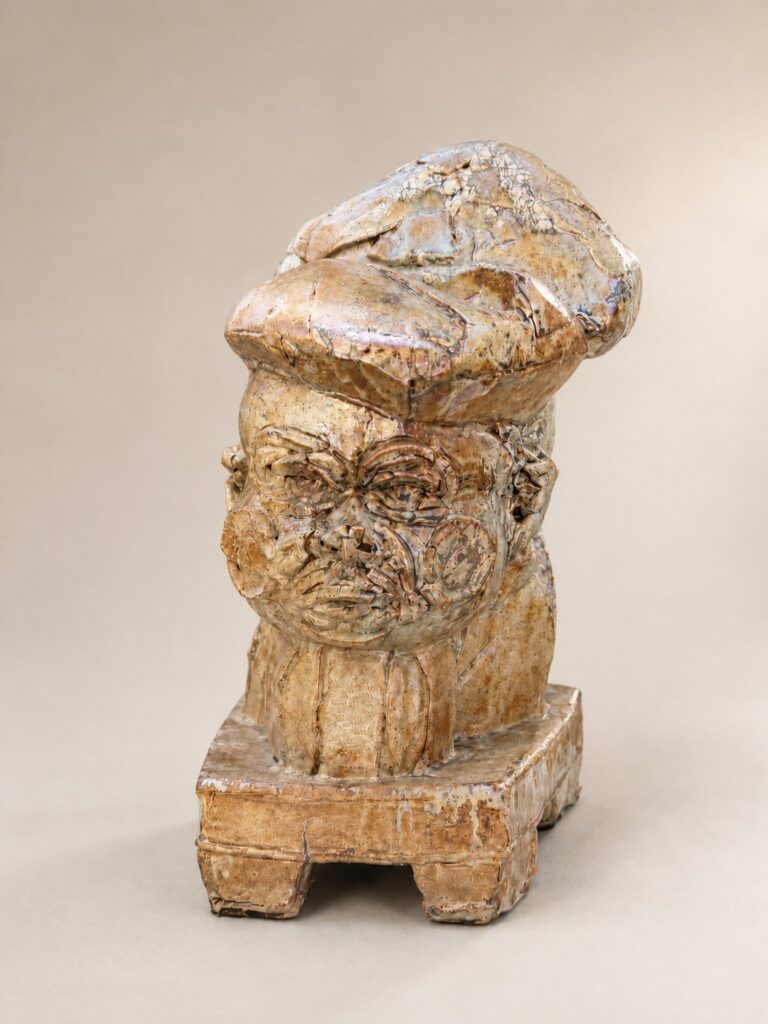 Head in a hat on a pedestal, tan glaze. Ceramic sculpture by Ted Fullwood